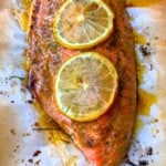 Baked salmon filet on pan with lemon slices on top.
